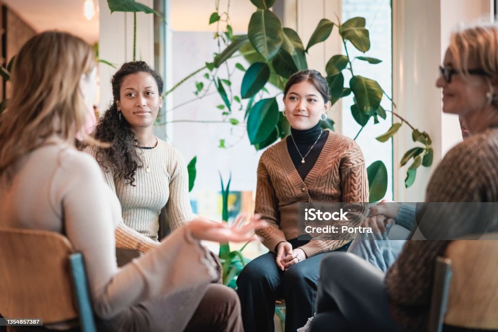 Woman sharing her experiences during a group therapy session Woman sharing her experiences during a mental health group therapy meeting. Multiracial women participate in support group session sitting in a circle. Group Therapy Stock Photo