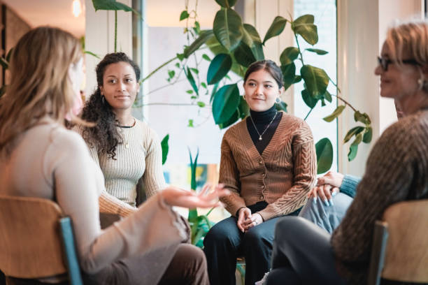 Woman sharing her experiences during a group therapy session Woman sharing her experiences during a mental health group therapy meeting. Multiracial women participate in support group session sitting in a circle. small group of people stock pictures, royalty-free photos & images