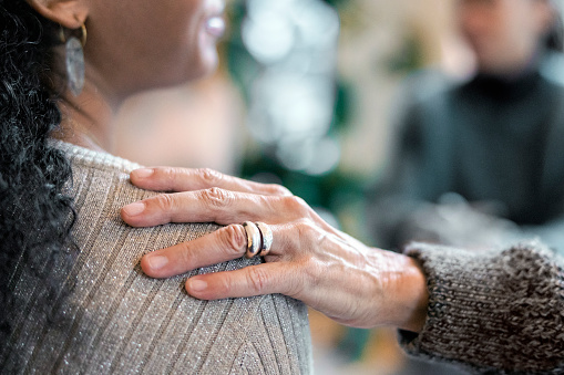 Close-up of a woman consoling a attendee during a mental health therapy session. Hand of a therapist on shoulder supporting a desperate female during group therapy session.