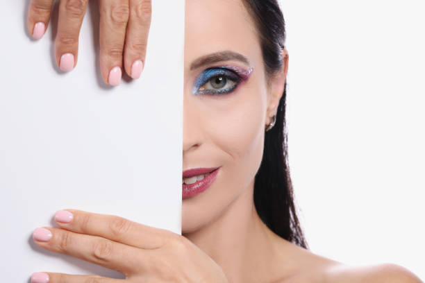 Portrait of woman with evening make-up covers half of face with white sheet Portrait of woman with evening make-up covers half of face with white sheet. Makeup training for yourself concept person holding frame over face stock pictures, royalty-free photos & images
