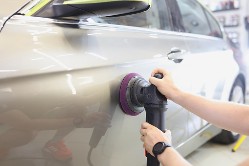 Craftsman polishes car door with eccentric sander in car service. Car polishing technology concept
