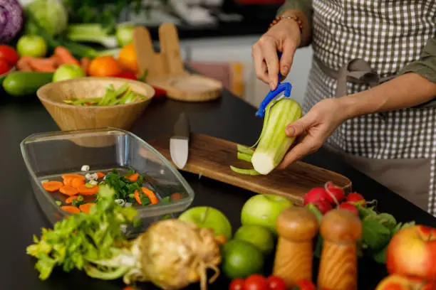 Midsection of unrecognizable woman standing over a kitchen counter and peeling a zucchini for a healthy meal she is preparing.