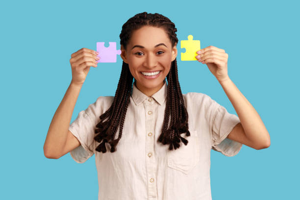 istock Woman with black dreadlocks showing to camera two pieces of puzzles, solving task. 1354858962