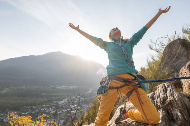 female mountain climber arms outstretched on mountain top - conquering adversity wilderness area aspirations achievement imagens e fotografias de stock