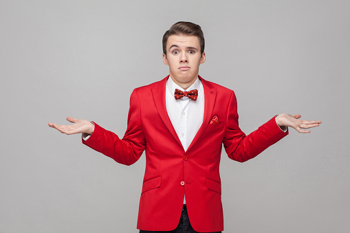 I don't know! Portrait of puzzled confused gentleman with stylish hairdo in red tuxedo and bow tie shrugging shoulders in bewilderment with grimace who cares, so what. studio shot, gray background