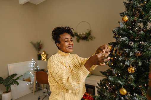 Photo of a smiling woman decorating her Christmas tree at home
