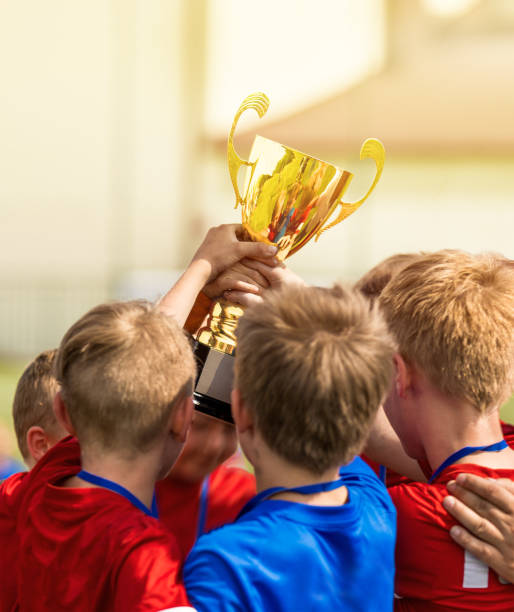 gruppo di ragazzi felici in magliette sportive rosse e blu raccogli la coppa d'oro. school kids vince il campionato sportivo. torneo sportivo per bambini nella soleggiata giornata estiva - medal soccer success winning foto e immagini stock