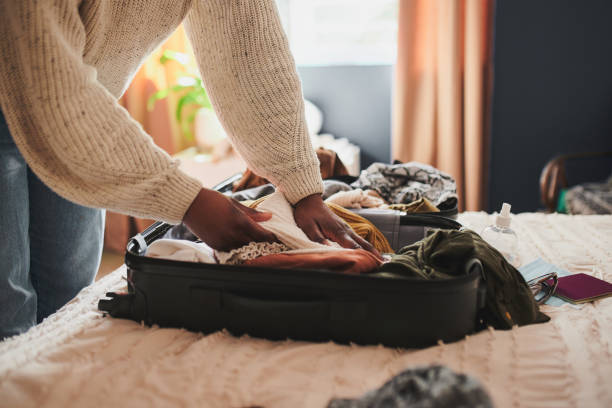 tiro cropped de uma mulher irreconhecível embalando suas coisas em uma mala em casa antes de viajar - mala de viagem - fotografias e filmes do acervo