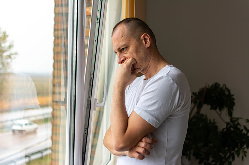 Feeling hopeless. Thoughtful man looking out the window in bedroom at home. Thoughtful man looking out the window. Lonely depressed man near window at home.