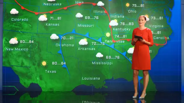 Photo of Live Weather News Studio with Professional Female On-Camera Meteorologist Standing Beside Screen and Making Gestures to Point at Weather Synoptic Map Chart for United States of America