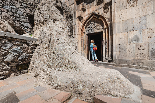 Woman visitor entering at the Geghard Monastery in Armenia. It is an important travel and religious pilgrimage point in Kotayk province