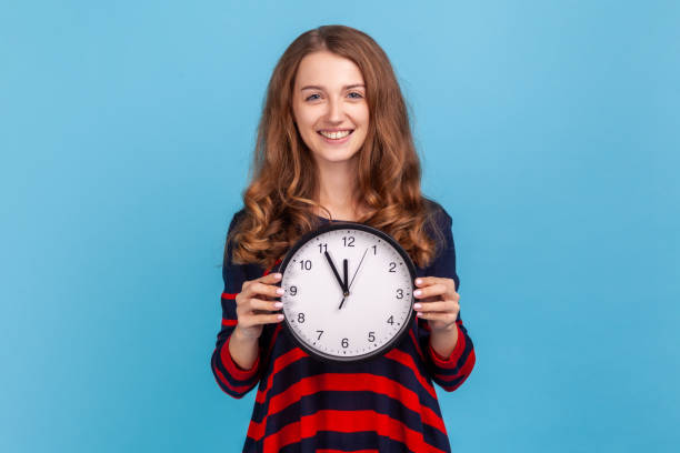 istock Woman holding clock, smiling to camera, expressing optimism, enough time, not hurry. 1354866547