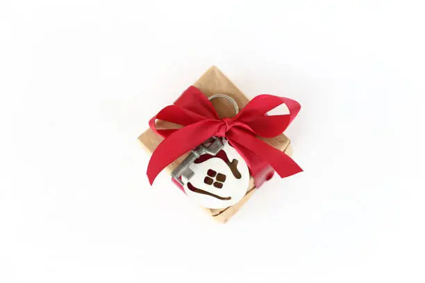 a gift in a box with a red bow, key and house on a light top view surface