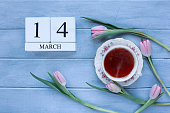 Steaming hot cup of tea and pink spring tulip flowers over a rustic blue wooden table