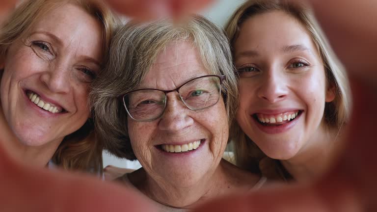 Three female generations look at camera through heart of fingers