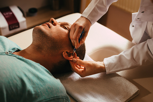 Man lying down in a clinic and having an acupuncture treatment on his ear