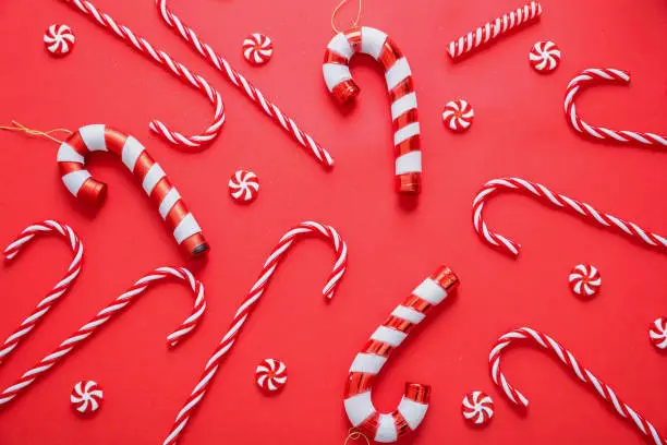 Merry Christmas. Candy canes on red background. Xmas flat lay, pattern. Peppermint red white striped traditional kids candies