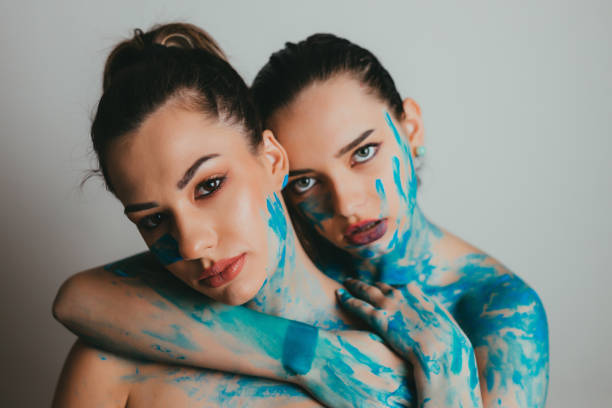 Portrait of two beautiful young women covered in blue body paint, studio shot in front of white background