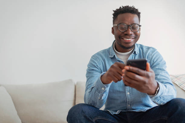 istock Cheerful businessman using smartphone while sitting on sofa at home. 1354876745