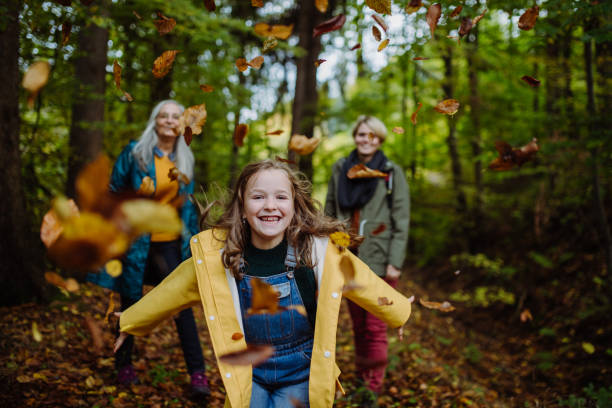 счастливая маленькая девочка бегает и бросает листья во время осенней прогулки с мамой и бабушкой в лесу - action women beginnings autumn стоковые фото и изображения