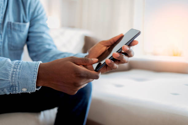 istock Cheerful businessman using smartphone while sitting on sofa at home. 1354877448