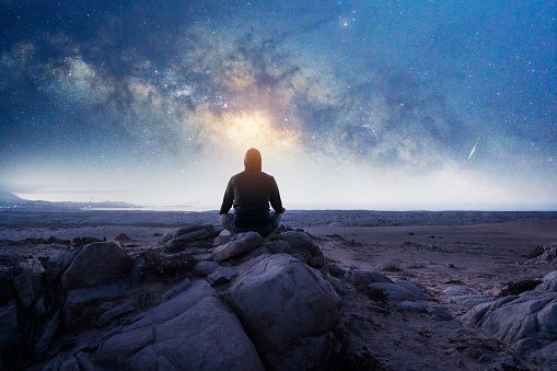 person sitting on the top of the mountain meditating or contemplating the starry night with Milky Way and Moon background in Atacama Desert