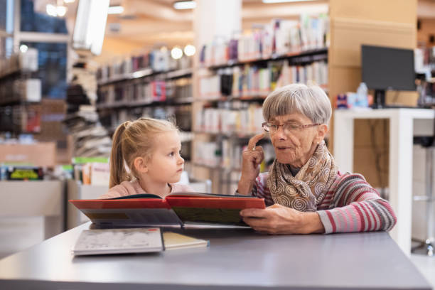 grandmother reads a book to her granddaughter in the library - grandparent reading grandmother child imagens e fotografias de stock