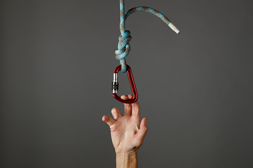 Hand grasping onto a climbing rope with carabiner as safety concept, against a grey background.