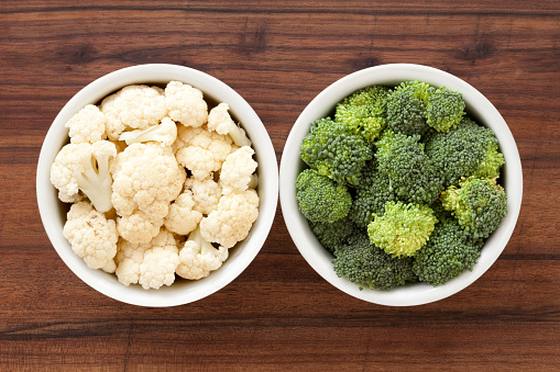Top view of two bowls side by side with cauliflower and broccoli