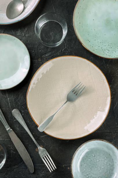 istock Modern tableware on a dark background. A plate with a fork and a glass, top shot 1354888333