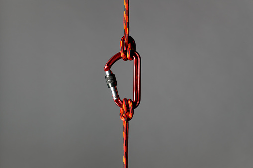 Climbing rope with carabiner as safety concept against a grey background.