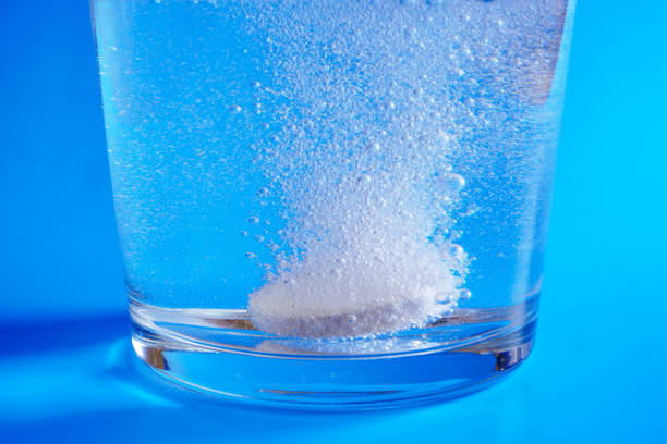 青い背景に水のガラスに溶解発泡錠のクローズアップ - 発泡錠 ストックフォトと画像