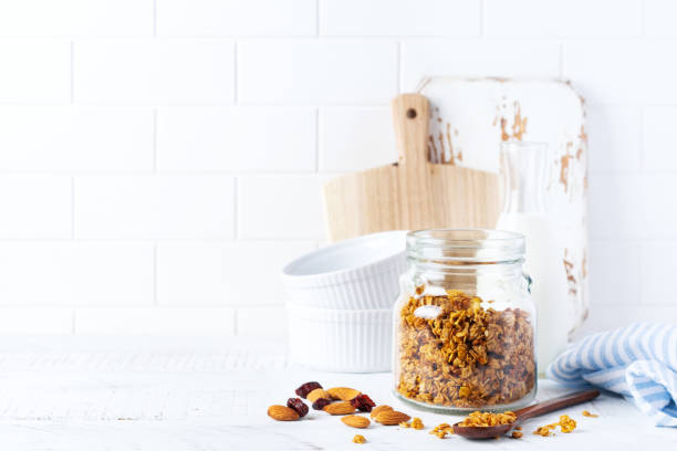 granola d’avoine avec des noix et des fruits secs pour préparer un petit-déjeuner sain sur une table de cuisine lumineuse. style blanc scandinave. focalisation sélective - spoon honey cute jar photos et images de collection