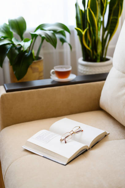 istock Opened paper book with glasses on a beige sofa. 1354891496