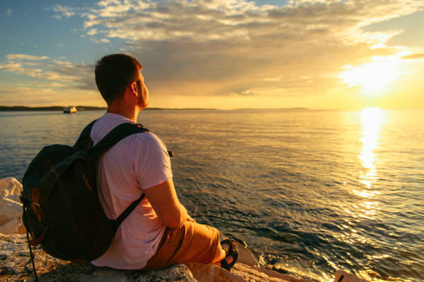 istock man with backpack enjoying sunset over the sea 1354891738
