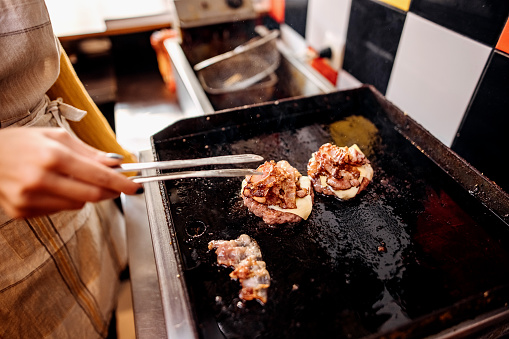 Woman working in a grilled fast food restaurant prepares a burger