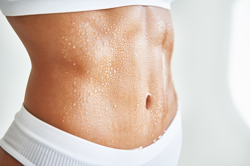 Close up belly of a beautiful sporty girl in drop of sweat or water on skin. Body care, fitness concept