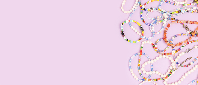 Necklaces and bracelets made from multicolored beads and pearls on a purple background with copyspace.