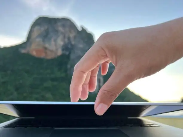 Photo of Hand opening a MacBook during the holiday against blur Mountain and sky