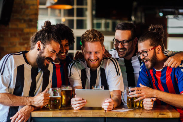 Group of friends watching the football game at the pub Multi - ethnic group of football fans watching a basketball game on the tablet and drinking beer at the pub. sports betting stock pictures, royalty-free photos & images