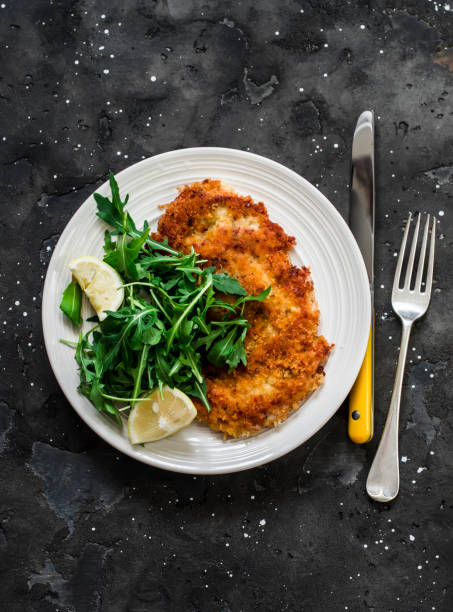 Garlicky bread crumbs crispy turkey schnitzel and fresh lemon arugula salad on a dark background, top view Garlicky bread crumbs crispy turkey schnitzel and fresh lemon arugula salad on a dark background, top view schnitzel stock pictures, royalty-free photos & images