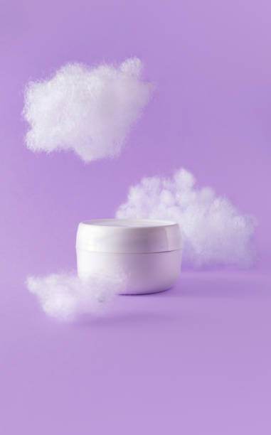 istock Moisturizer cream in jar with fluffy clouds on violet. Concept care with sensitive skin. Creative still-life photo, vertical 1354907184