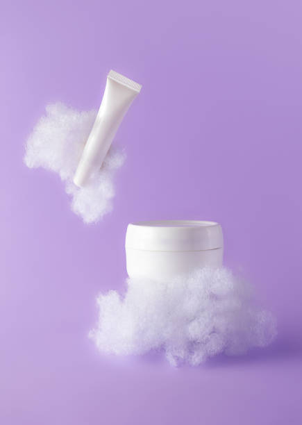 istock Facial cream and lip balm with fluffy clouds on violet background. Concept care with sensitive skin. Creative still-life photo, vertical. Template mockups beauty products 1354907254