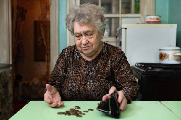 A sad elderly woman is counting money on the kitchen table. The concept of poverty, low income in old age. budget cut stock pictures, royalty-free photos & images