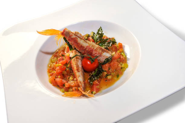 Goatfish or Red mullet in tomato sauce Goatfish or Red mullet in tomato sauce with parsley in white plate . Italian fish recipe called Triglie alla livornese. Isolated on white livorno stock pictures, royalty-free photos & images