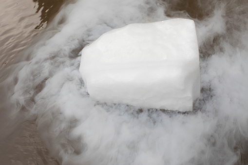 Dry ice evaporates in the water. Steam from a large piece of ice. Chemical experiment. Distribution of fog over water.