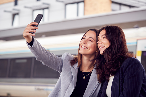 Businesswomen Commuting To Work Waiting For Train On Station Platform Taking Selfie On Mobile Phone