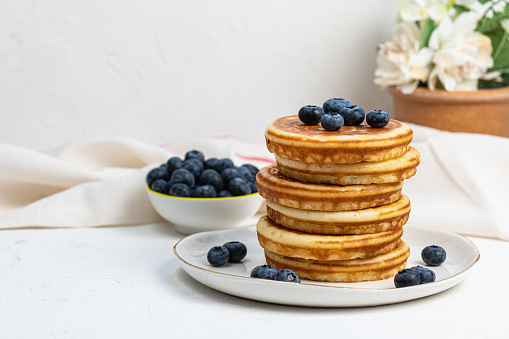 Stack of delicious pancakes on white plate with fresh blueberries. Frond view, Copy space