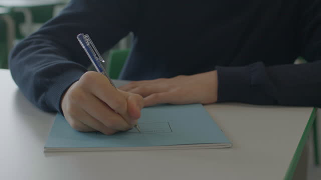 Schoolboy writing name on blue composition book