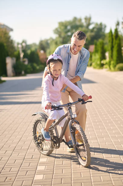 istock A man supporting a girl while she riding a bike 1354918047